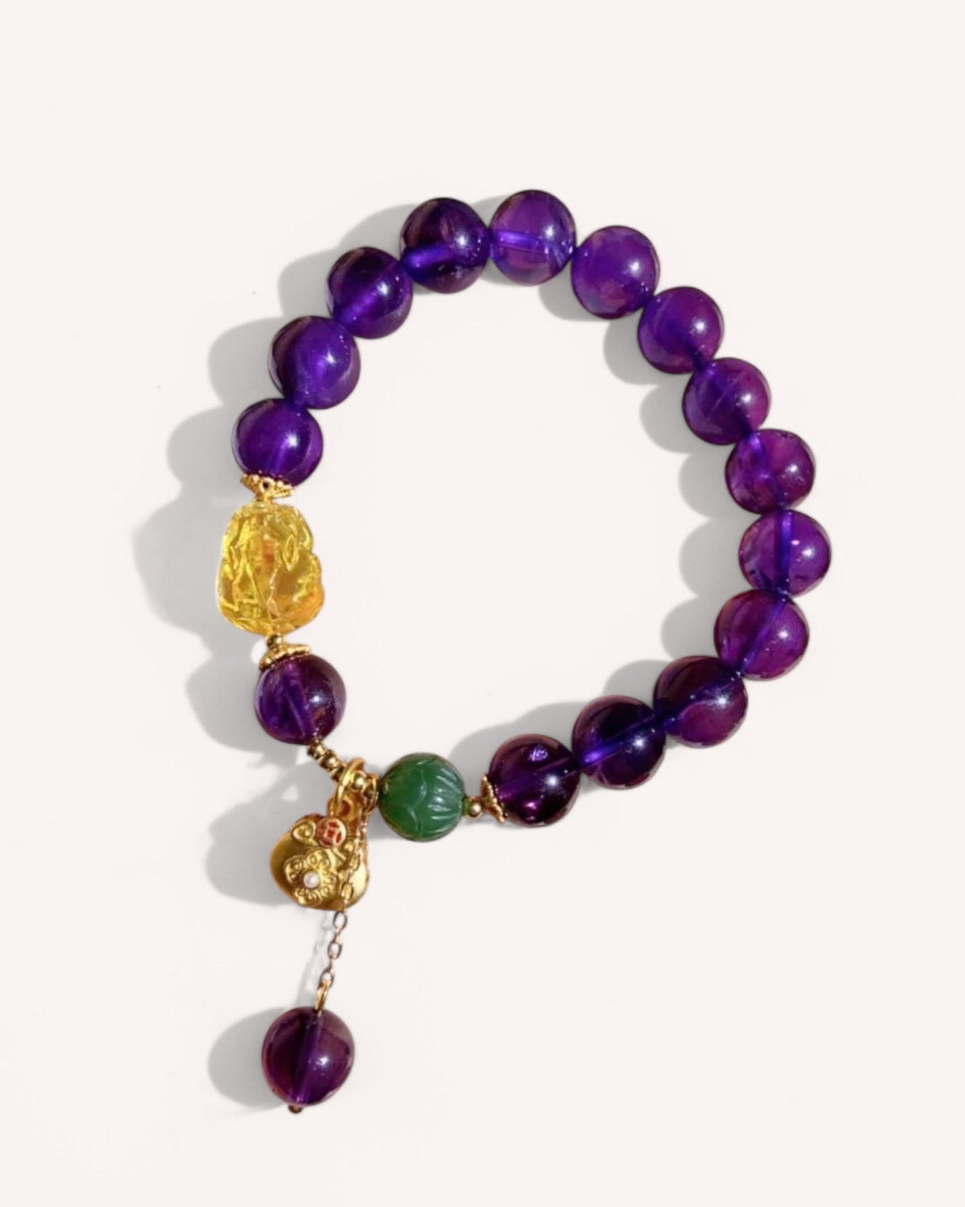 A deep purple amethyst bracelet with jade and Pixiu charm, symbolizing wealth, protection, and spiritual balance, photographed against a white background.