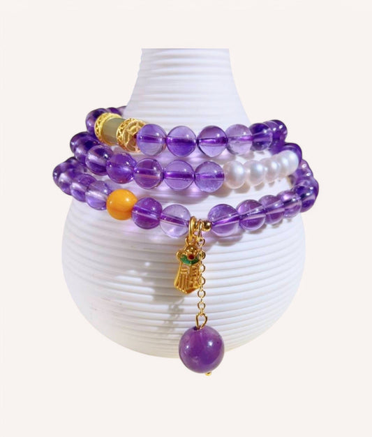 Amethyst & Honey Amber Prosperity Wrap Bracelet elegantly displayed on a decorative vase, showcasing its multi-layered design for abundance and emotional balance