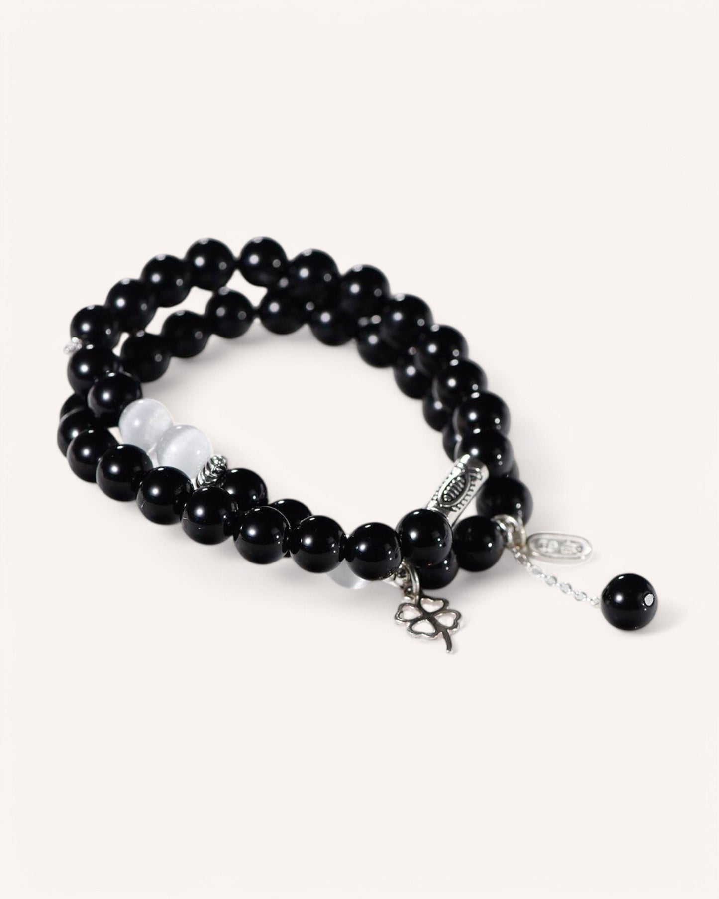 Flat-lay image of double-layer black crystal bracelet with Cat’s Eye and silver good luck charm