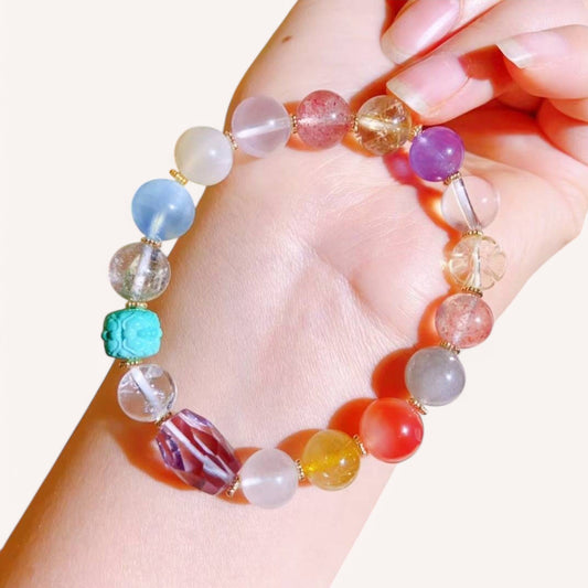 Hand wearing vibrant crystal bracelet with Rutilated Quartz, Aquamarine, and Strawberry Quartz for positivity, love, and intuition