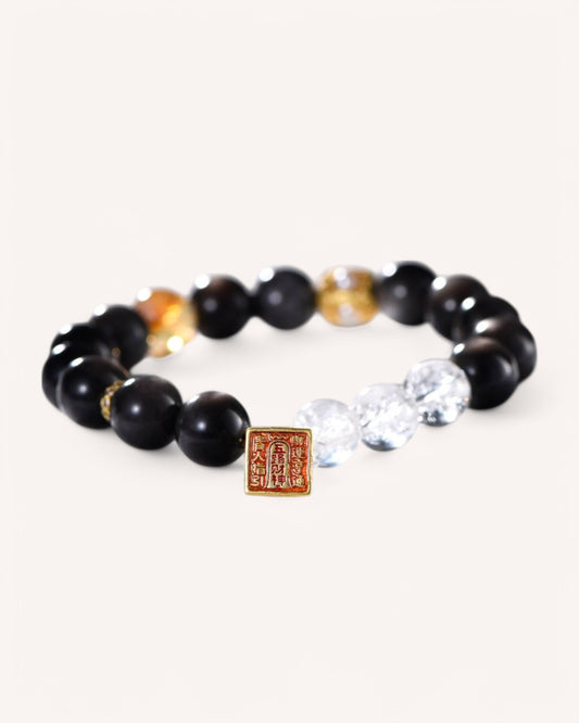 Side angle of wealth-attracting Silver Sheen Obsidian and White Quartz bracelet with Five Wealth Gods charm