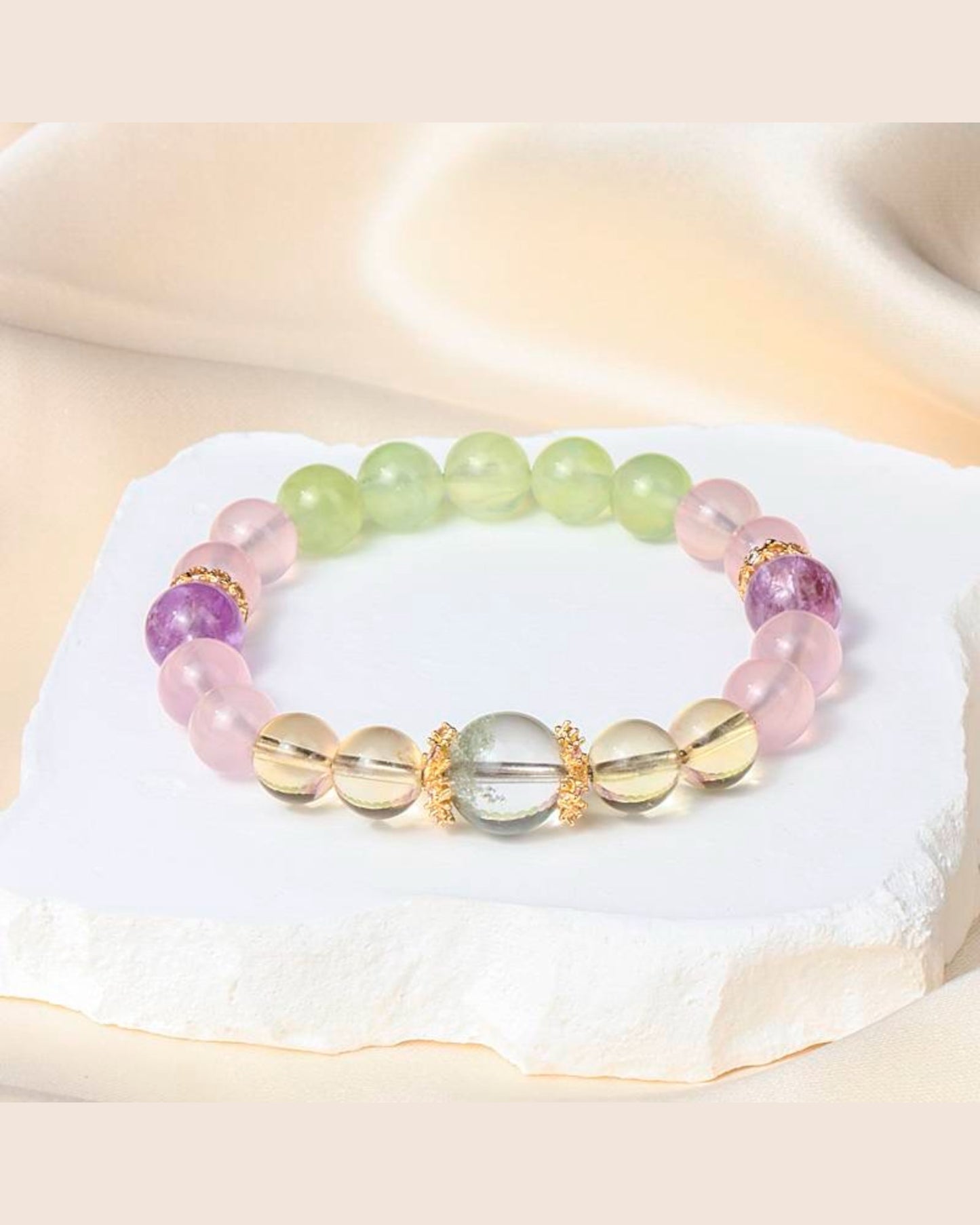 A stunning White Quartz, Amethyst, Rose Quartz & Prehnite bracelet placed on a white stone, symbolizing emotional healing, spiritual growth & protection.
