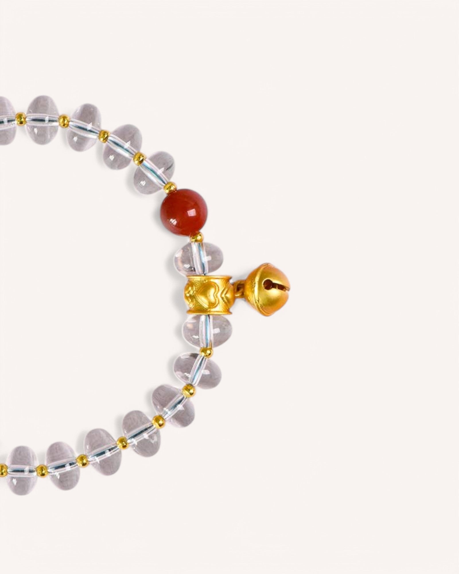 Top-down view of a white quartz energy bracelet with a gold bell and red coral, representing prosperity, wealth attraction, and emotional balance.