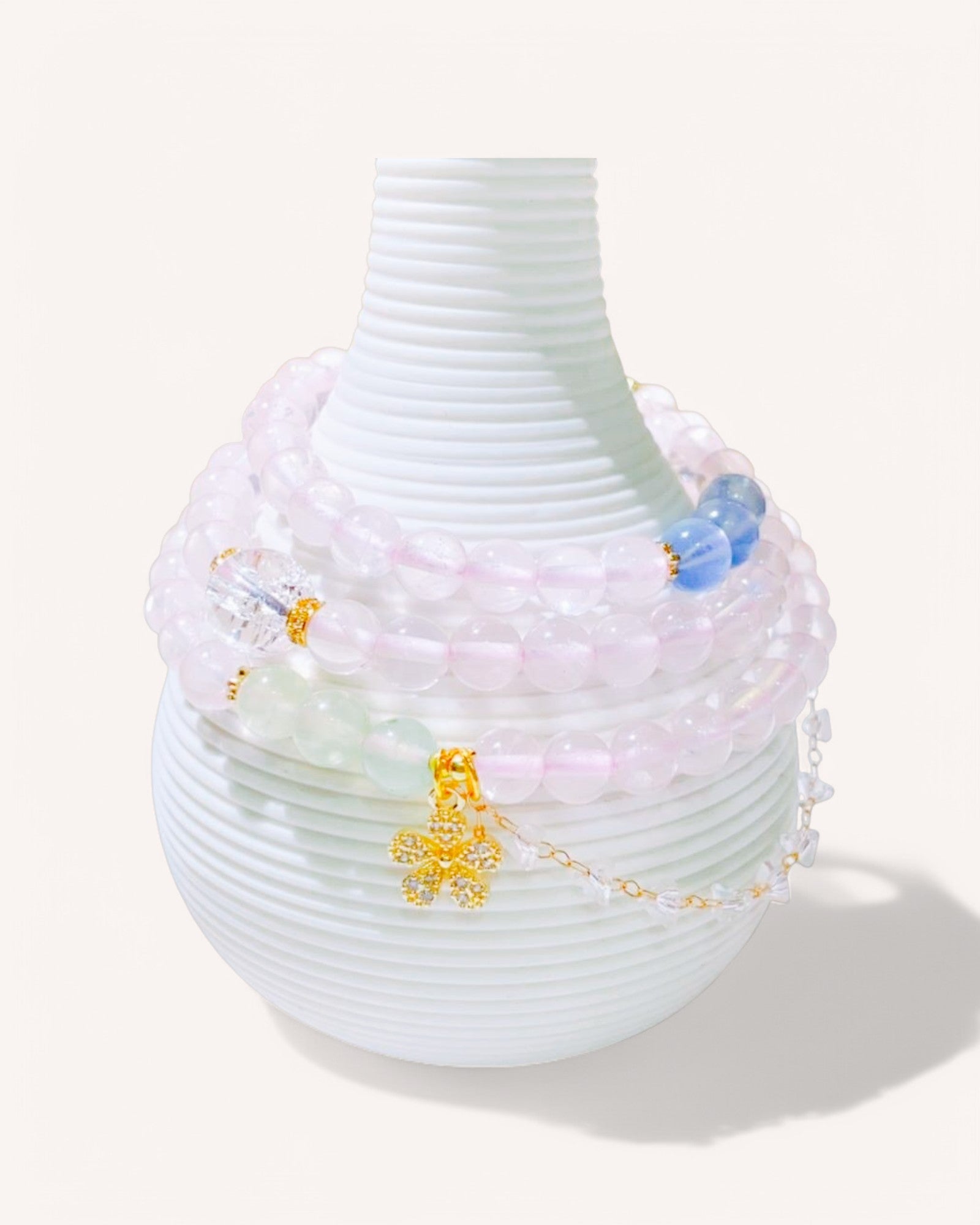 A delicate Rose Quartz multi-layer bracelet elegantly wrapped around a vase, featuring Golden Rutilated Quartz and a gold charm for love, clarity, and spiritual grounding.