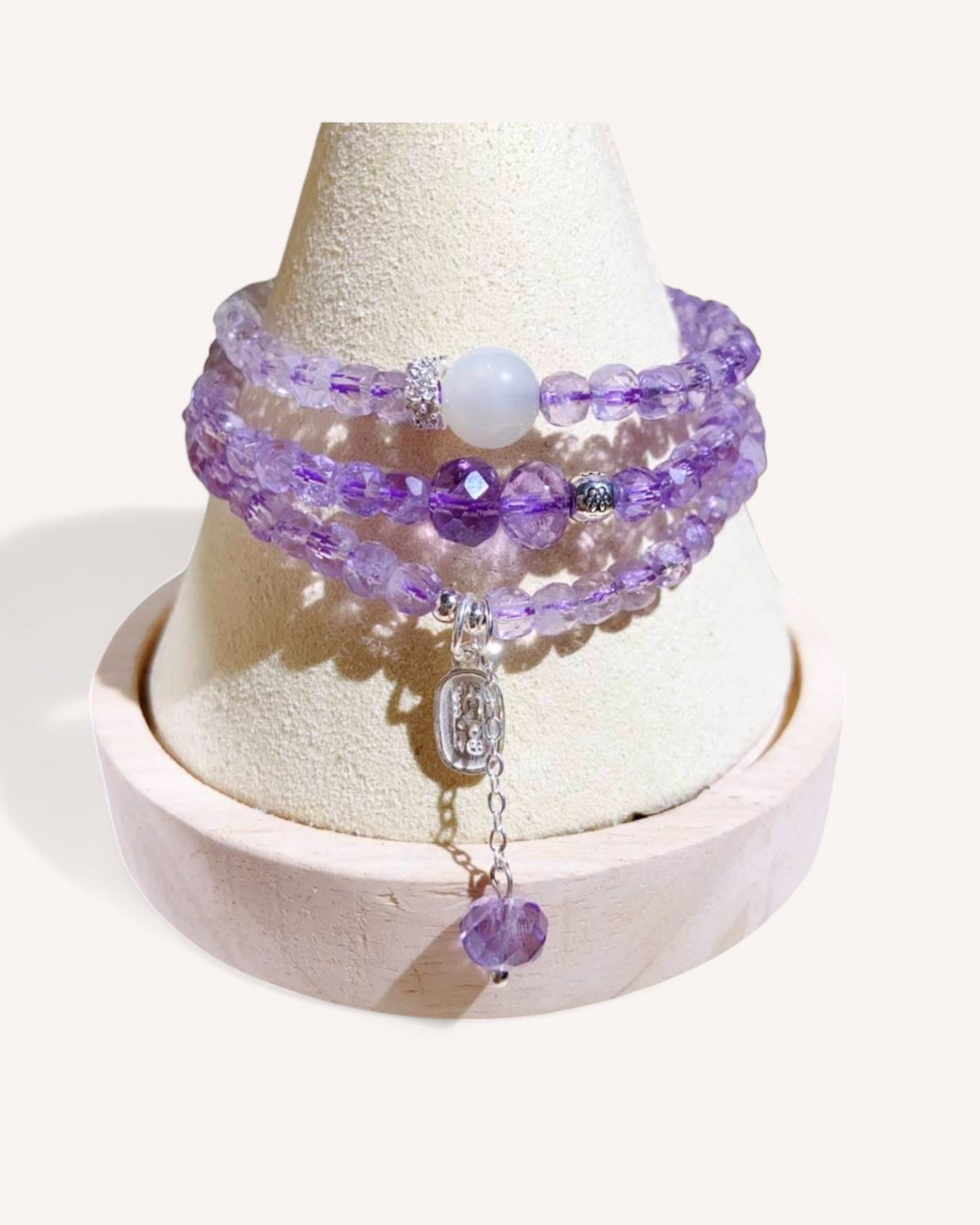 Amethyst Triple-Wrap Bracelet displayed on a jewelry stand, highlighting its handcrafted design with high-energy amethyst, white jade, and sterling silver. A powerful accessory for serenity, balance, and protection.