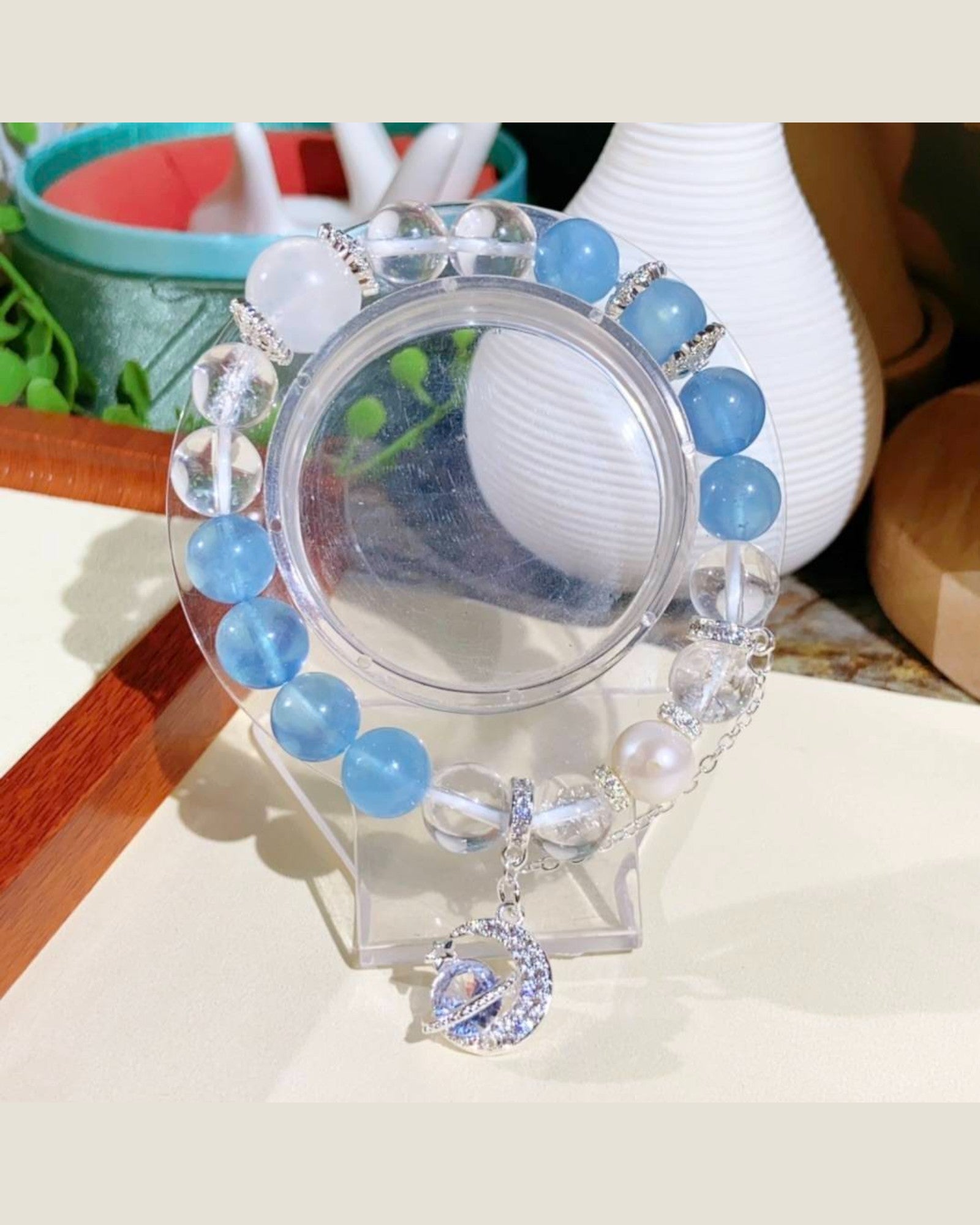 The Celestial Harmony Aquamarine & White Quartz Bracelet displayed on a stand, showcasing its calming aquamarine stones, white quartz energy amplifier, pearl for wisdom, and blue moonstone charm.