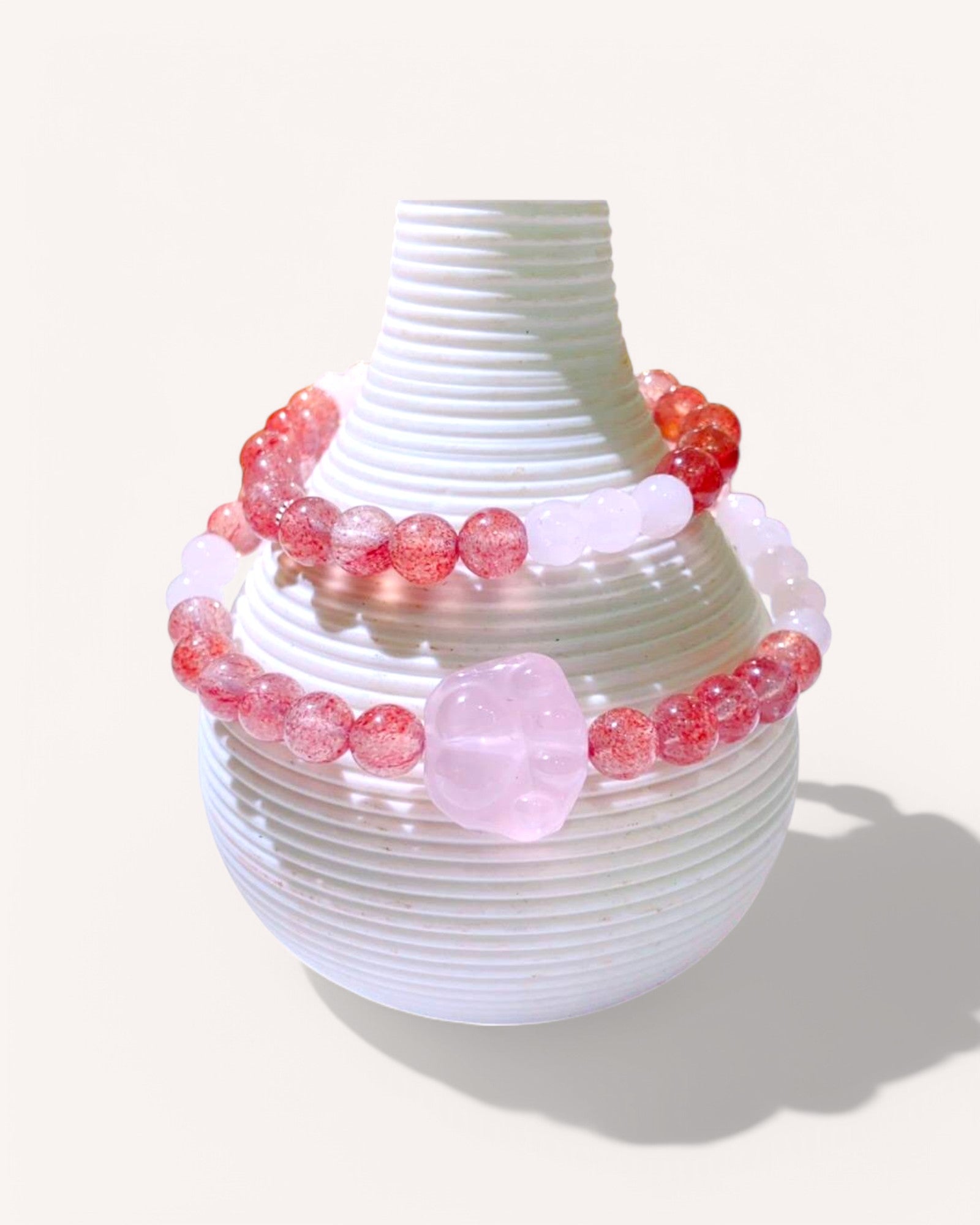 Strawberry Quartz and Rose Quartz heart crystal bracelet for love, healing, and emotional balance displayed on a white ceramic vase.