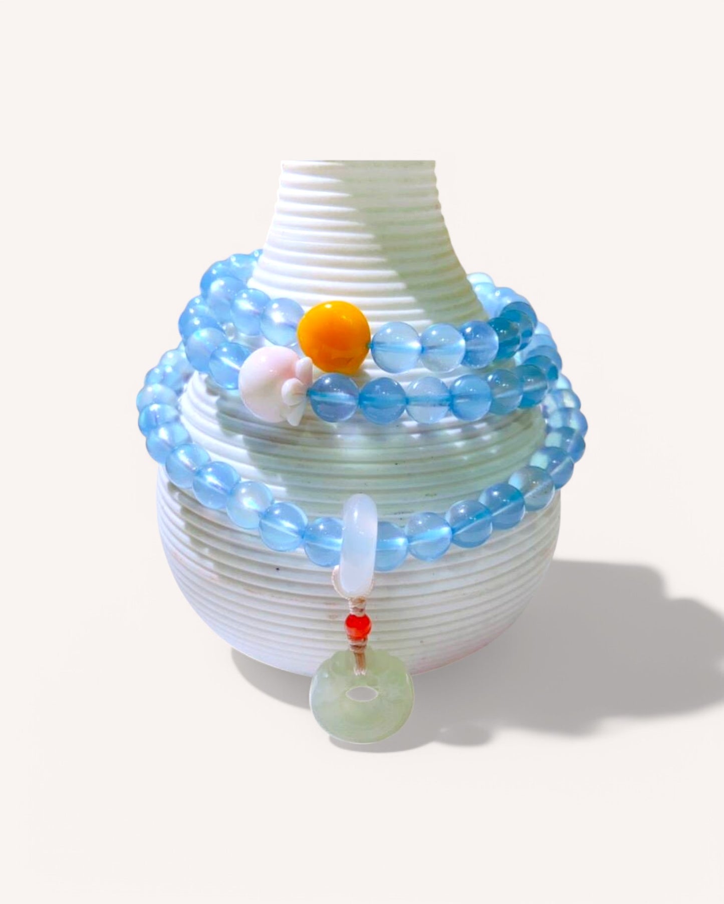 Triple-wrap aquamarine and jade gemstone bracelet displayed on ceramic vessel, symbolizing peace and grounding.