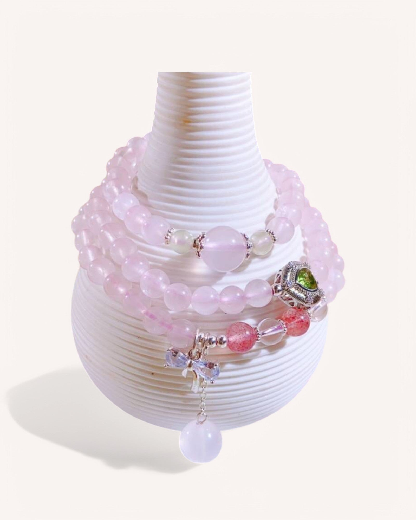Triple-layer rose quartz and strawberry quartz bracelet with grape stone and malachite copper charms displayed on a white vase for emotional healing and love.